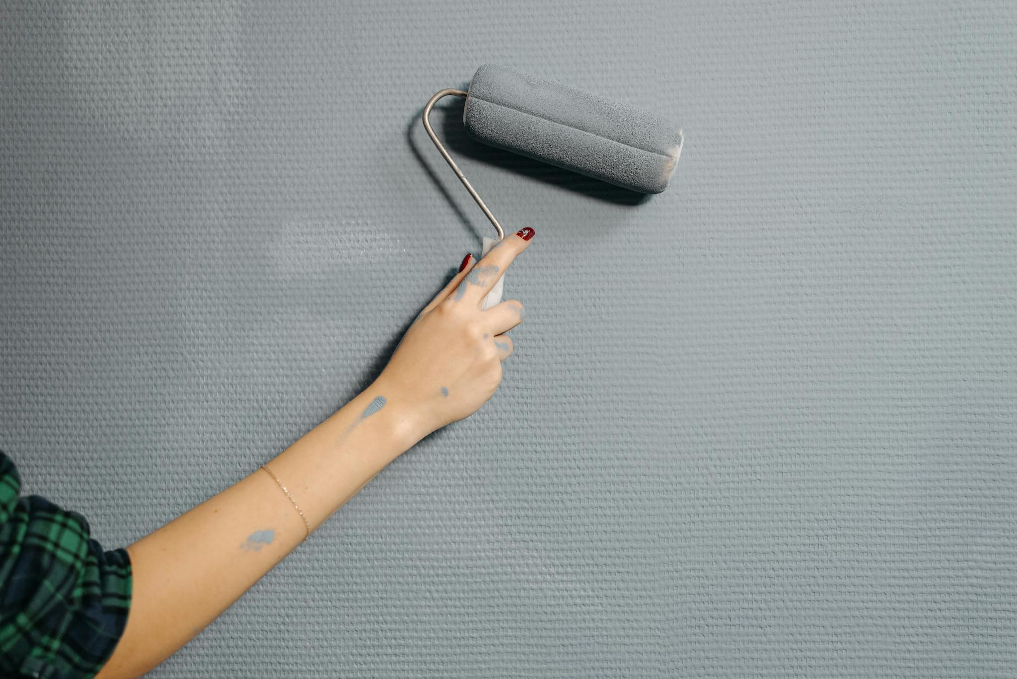 A close-up of a person's hand using a paint roller on a blue wall for home renovation.