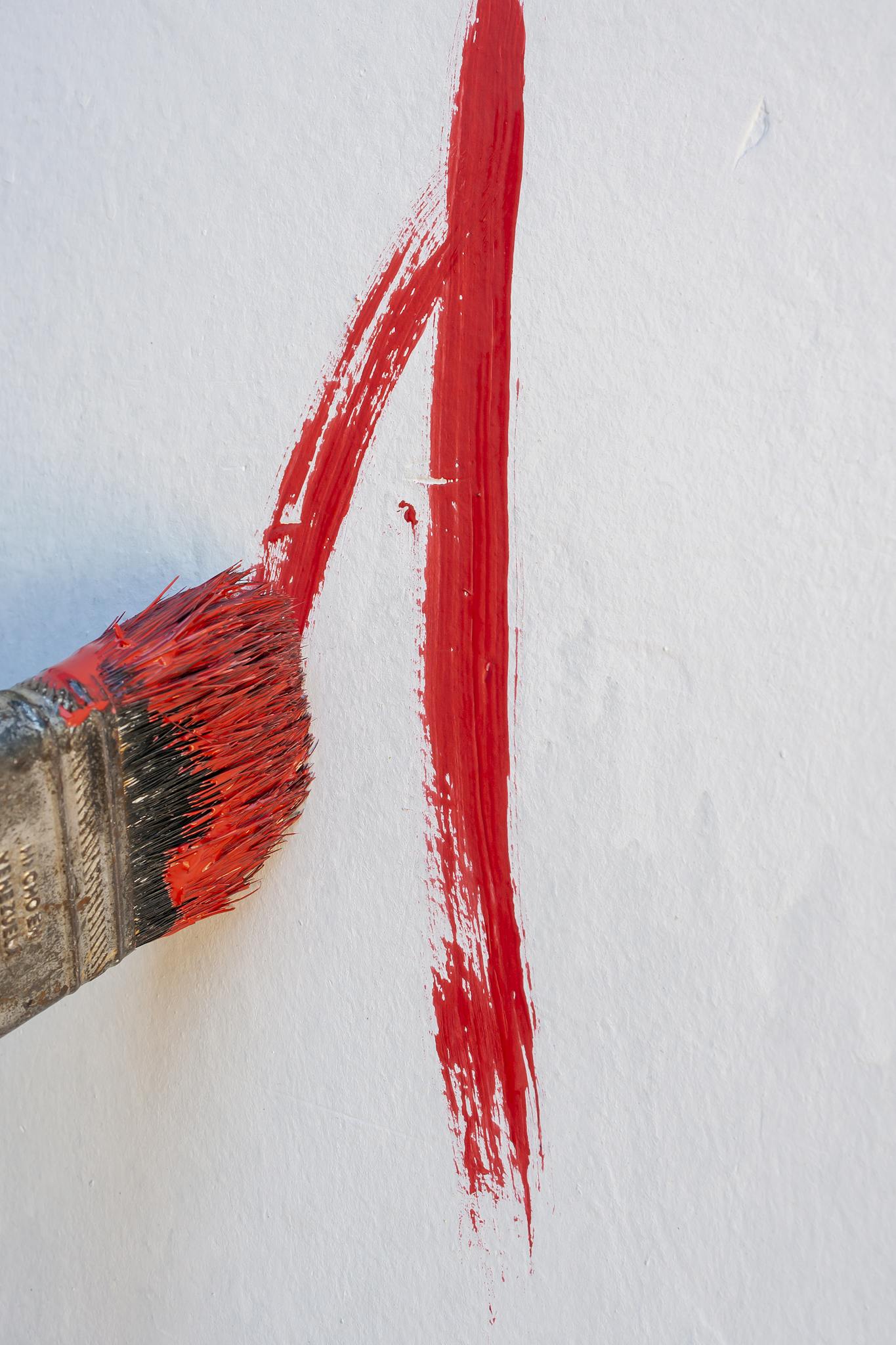 Close-up of a red paintbrush stroke on a white wall, emphasizing artistic creativity.